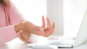Woman wearing pink sweater holding her wrist in pain at her desk